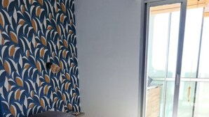Quarto com uma cama grande, cabeceira estampada e porta de vidro deslizante para uma varanda.