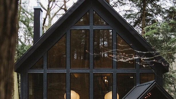 Une cabane moderne dotée de grandes fenêtres, d’une terrasse en bois et d’un intérieur chaleureux.