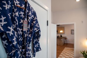 Een gang met een blauwe badjas aan een deur, leidend naar een keuken met houten vloer en een geruit patroon.