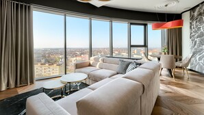 Een moderne woonkamer met een grote bank, een ronde salontafel en een uitzicht op een stadsbeeld door grote ramen.
