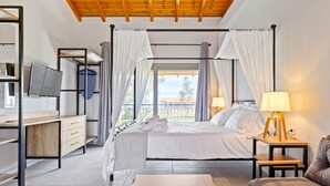 A modern bedroom with a bed, bedside tables, a desk, a TV, and a view of the outdoors. - Comissa Luxury Suites (Corfu)