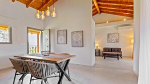 A modern dining area with a wooden table and chairs, framed artwork on the walls, and a cozy seating area with a sofa. - Comissa Luxury Suites (Corfu)