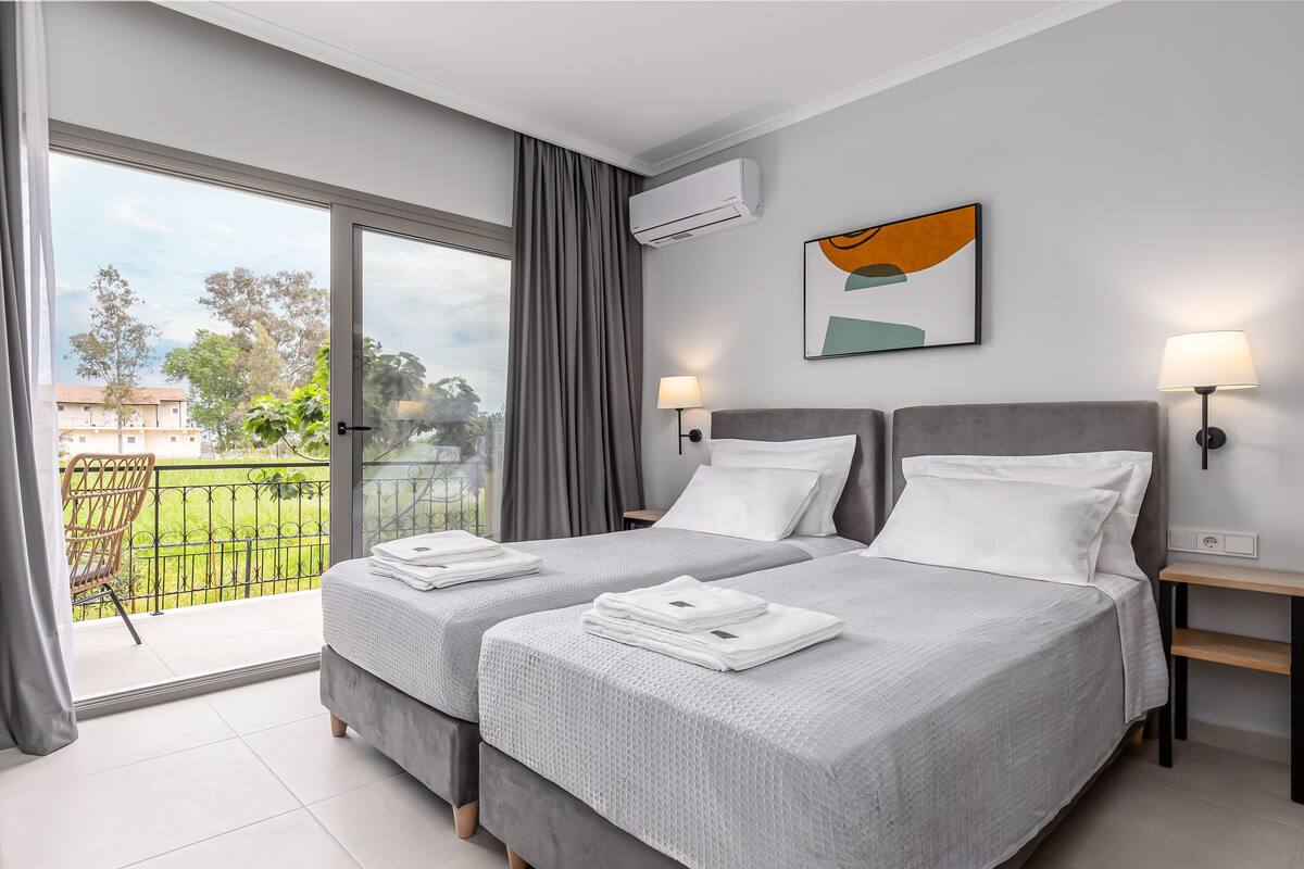 A modern hotel room with two beds, a balcony, and a view of the outdoors.