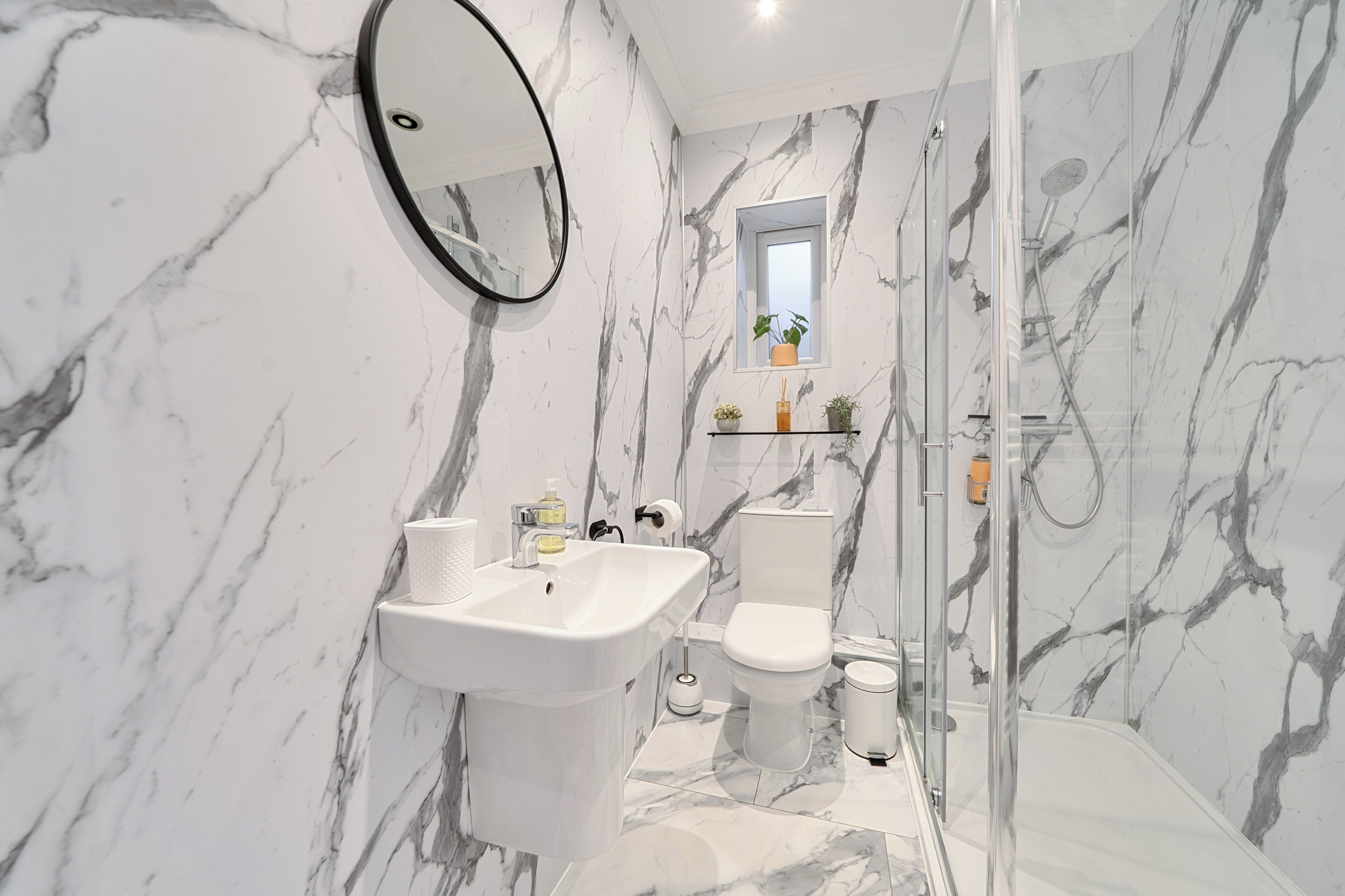 A bathroom with a marble wall, a sink, a toilet, and a shower.