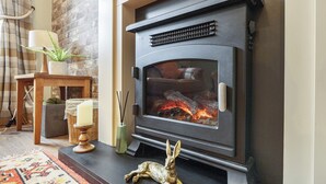 A wood-burning stove with a glass door, a decorative rabbit figurine, and a candle on a wooden stand.