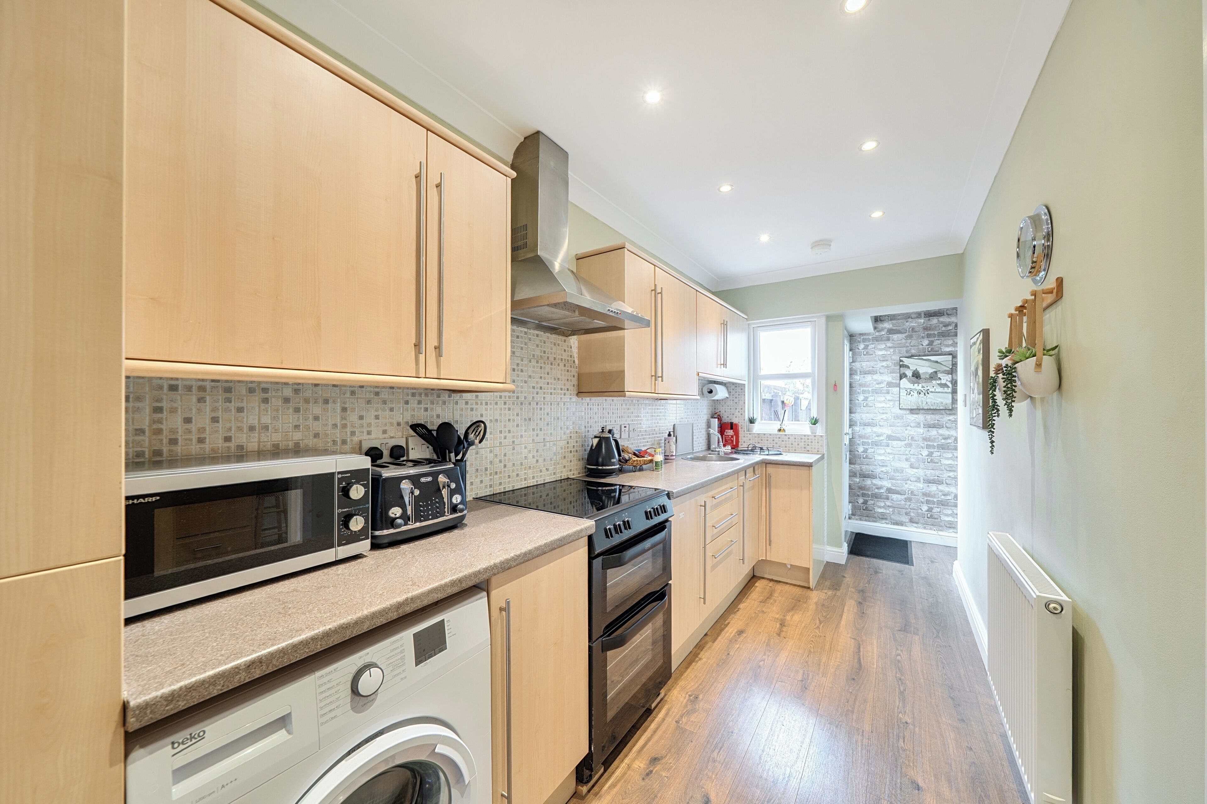 A modern kitchen with wooden cabinets, a built-in microwave, a stove, and a washing machine.