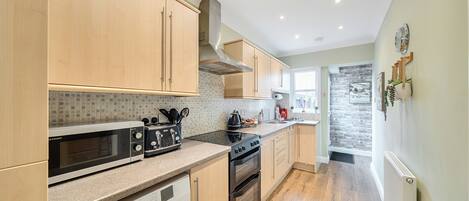 Una cocina moderna con armarios de madera, microondas integrado, estufa y lavadora.