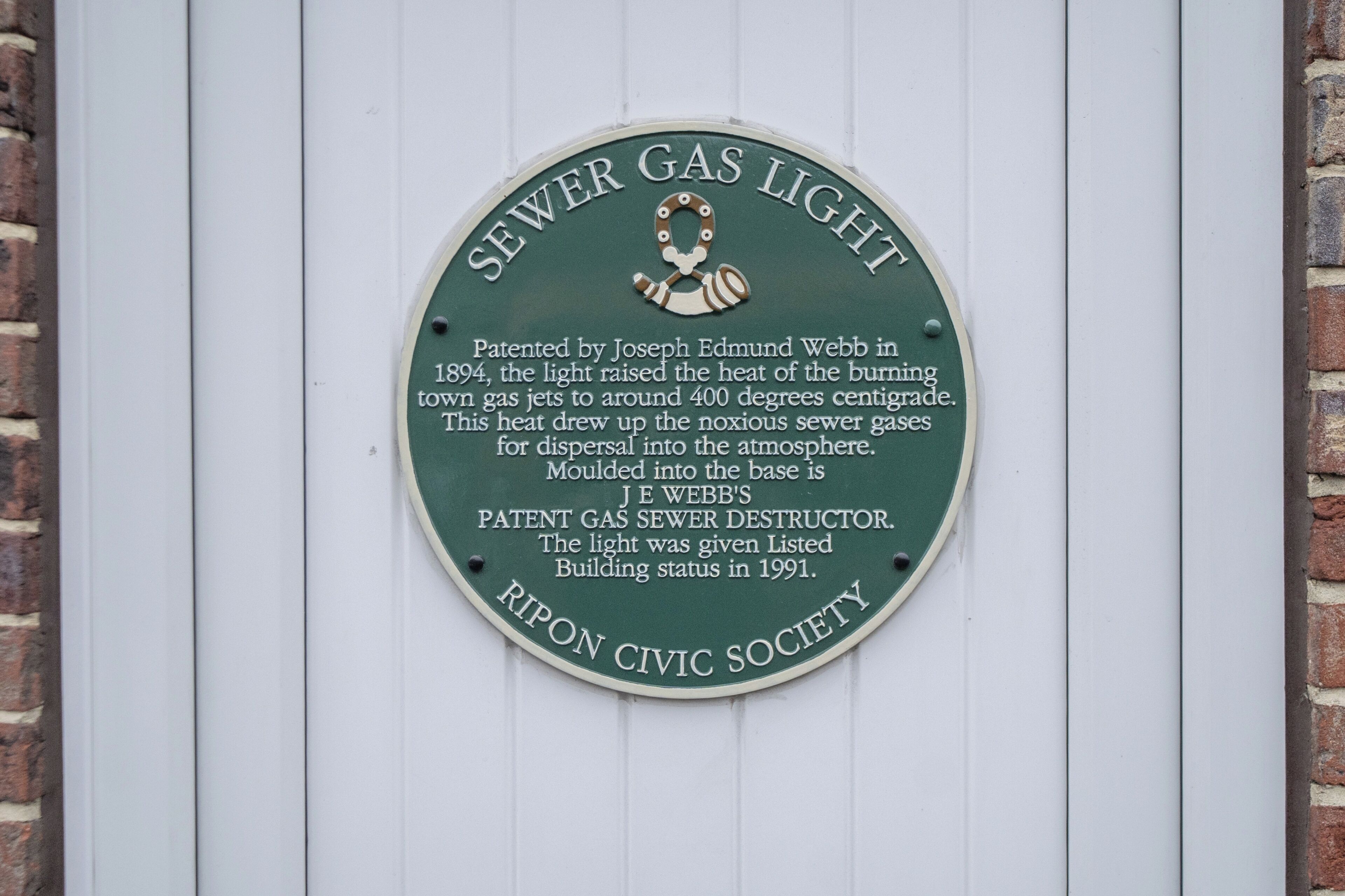 Placa na parede detalhando a invenção de Joseph Edmund Webb de uma lâmpada para gás de esgoto em 1894, patenteada em 1894 e listada como edifício em 1991.