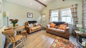 A cozy living room with a brown leather sofa, a wooden dining table, and a patterned rug.