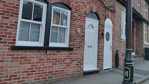 A brick building with two white-framed windows and a white door, a street lamp, and a plaque on the wall.