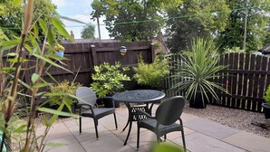 A patio area with a round table and two chairs, surrounded by potted plants and a wooden fence.