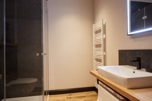 Uma casa de banho moderna com cabine de duche em vidro, uma sanita branca com torneira preta e um lavatório de madeira.
