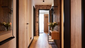 Un couloir aux murs en bois et un mur d’accent en briques, qui mène à une porte. Des bouquets de fleurs sont disposés sur des étagères et un tapis recouvre le sol.