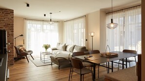 Un salon moderne avec un canapé, une table à manger et des chaises. On y trouve un mur en briques, de grandes fenêtres avec des rideaux légers et des luminaires suspendus.