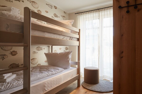 A bunk bed room with a round ottoman and a window with sheer curtains.