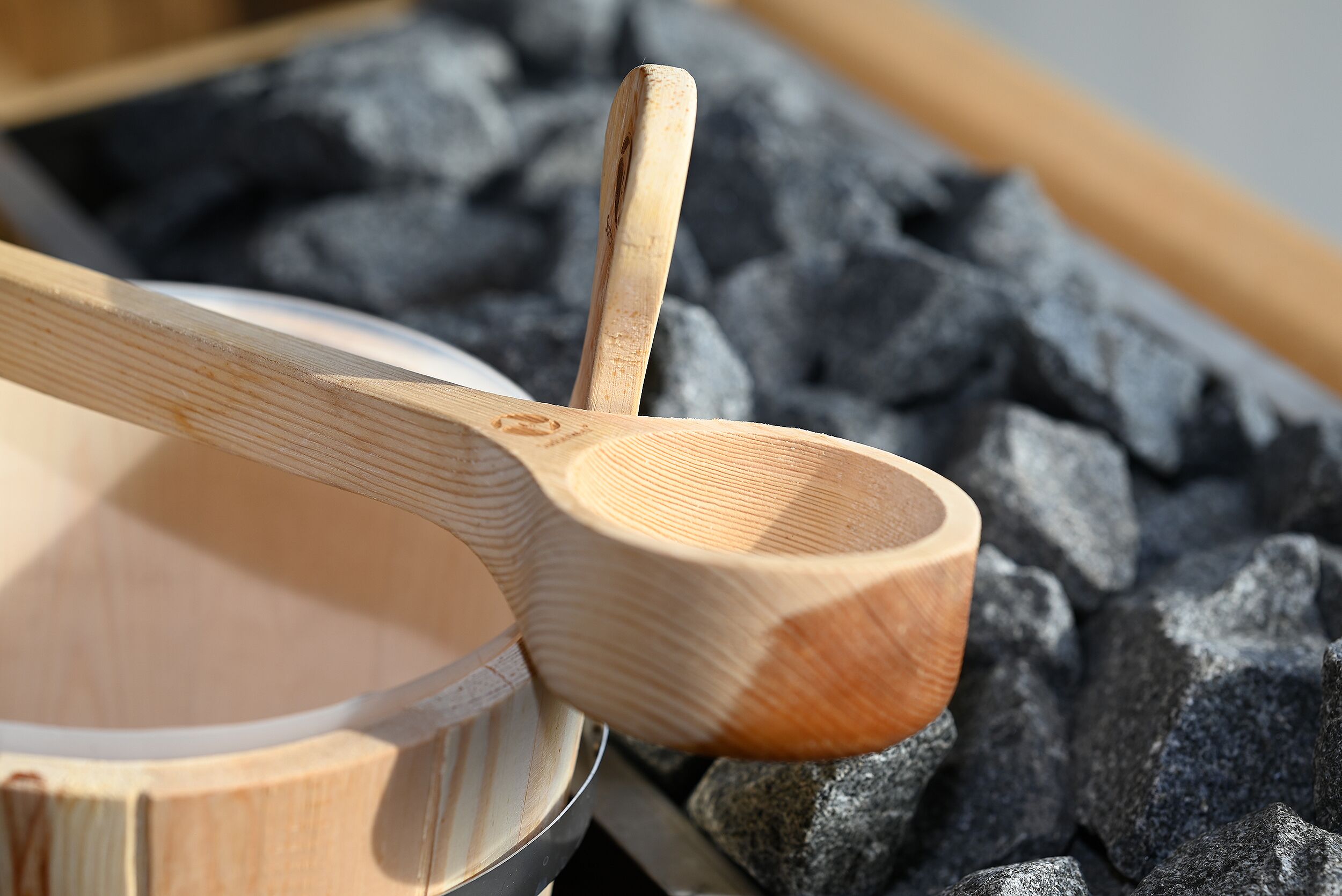 A wooden spoon resting on a bowl with a blurred background of black stones.