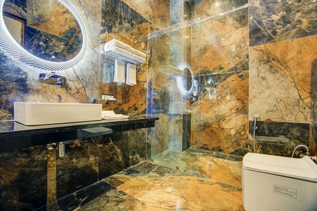 A modern bathroom with a marble floor, a glass-enclosed shower, a white sink, and a large mirror.