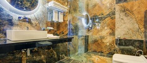 A modern bathroom with a marble floor, a glass-enclosed shower, a white sink, and a large mirror.