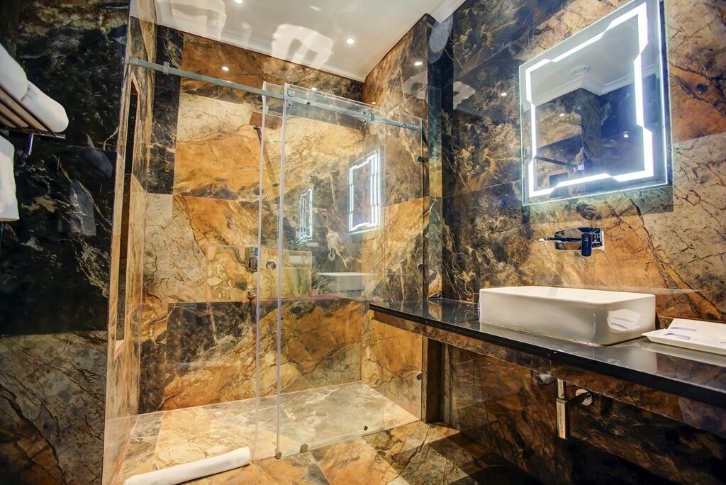 A modern bathroom with a glass-enclosed shower, marble walls, and a large mirror with integrated lighting.