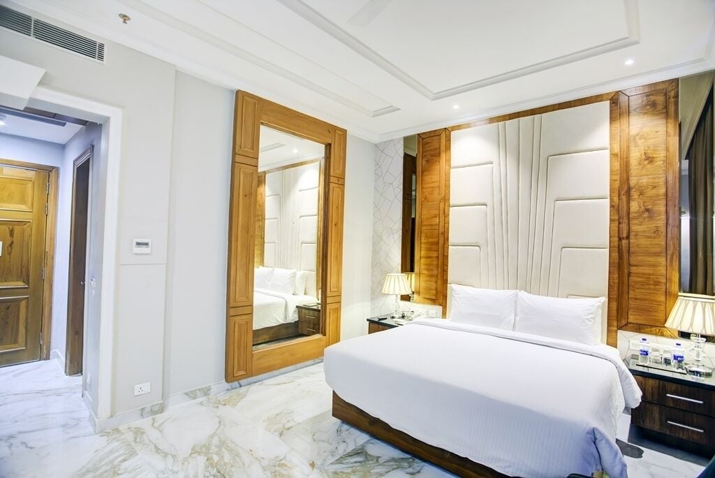 A hotel room with a large bed, wooden wardrobe, and a mirror.