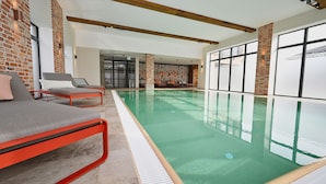 Piscina interna com design moderno, apresentando área de estar emoldurada em vermelho e grandes janelas.