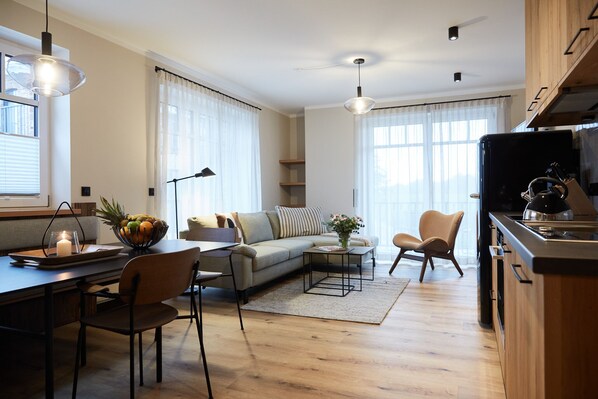 A modern living room with a sofa, coffee table, and chairs. There is a kitchen area with a stove and cabinets.