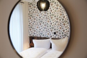 Vista circular de um quarto com cabeceira de madeira, roupa de cama branca e parede decorada com padrão de concha.