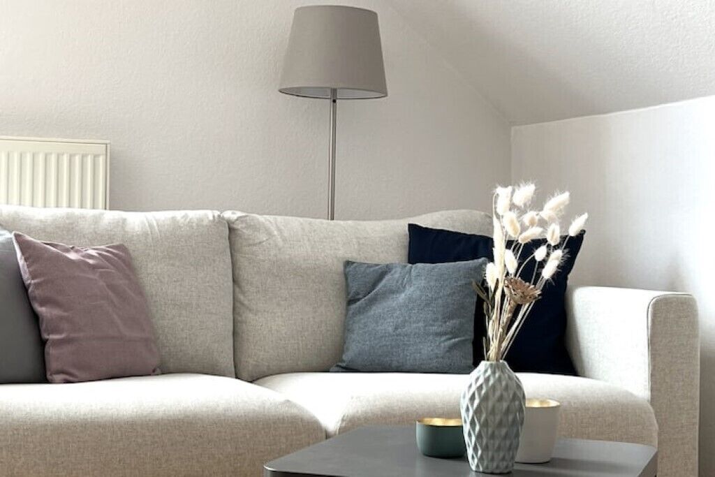 Ein Wohnzimmer mit einer Couch, einer Lampe und einer Tischvase mit getrockneten Blumen.