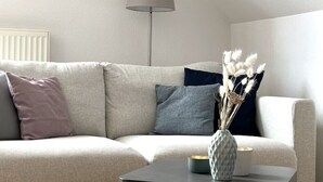 A living room with a sofa, a lamp, and a vase with dried flowers on a table.