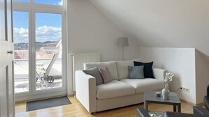 A modern living room with a white sofa, a small table, and a view of the city through large windows.
