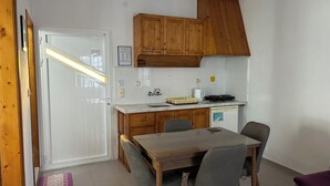 A compact kitchen with wooden cabinets, a white countertop, and a dining table with chairs. - Ege Apartments (Bodrum)