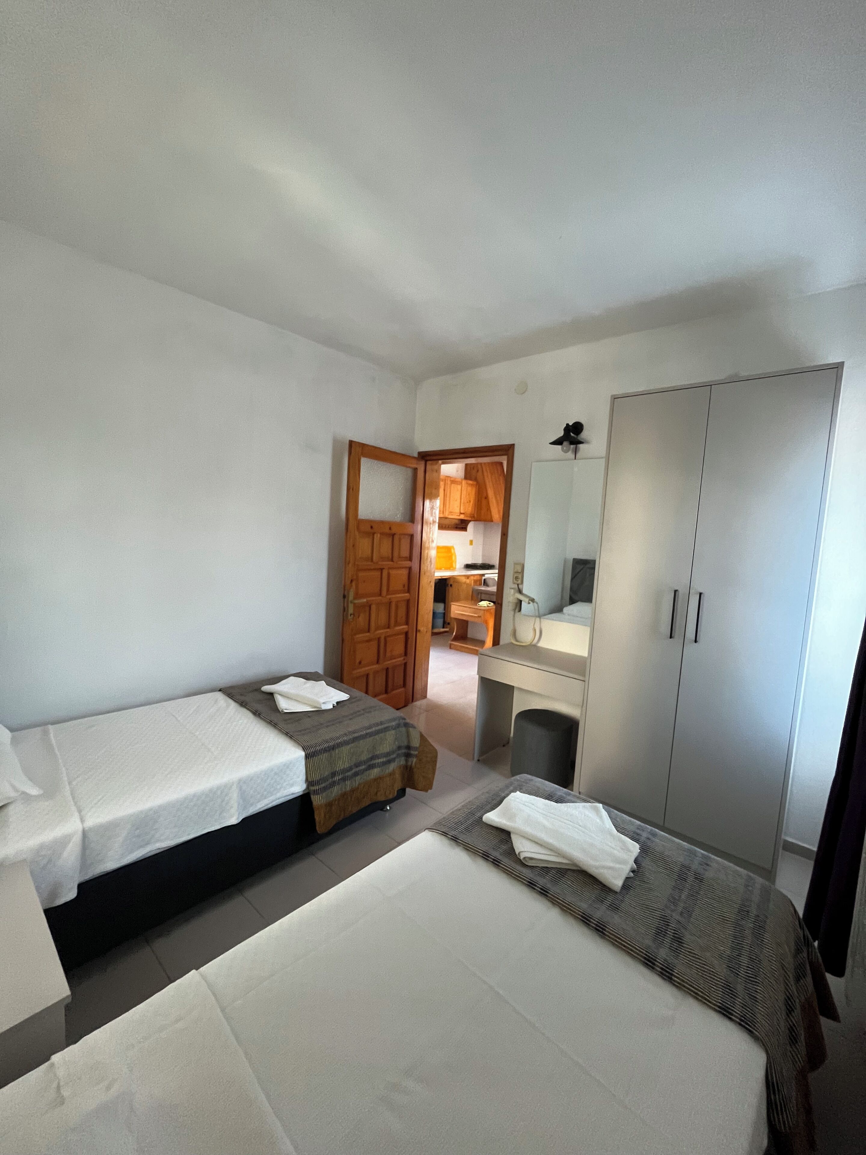 A hotel room with two beds, a wardrobe, a desk, and a bathroom visible through an open door.