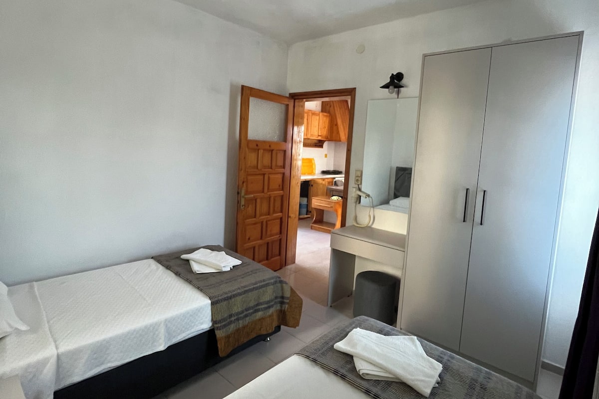 A hotel room with two beds, a wardrobe, a desk, and a bathroom visible through an open door.