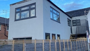 A modern two-story house with a grey facade, large windows, and a wooden fence in front.