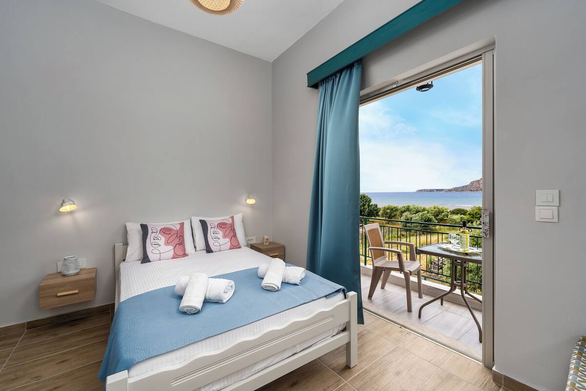 Une chambre à coucher comprenant un lit, une table de chevet, une table avec des chaises et un balcon avec vue sur la mer.