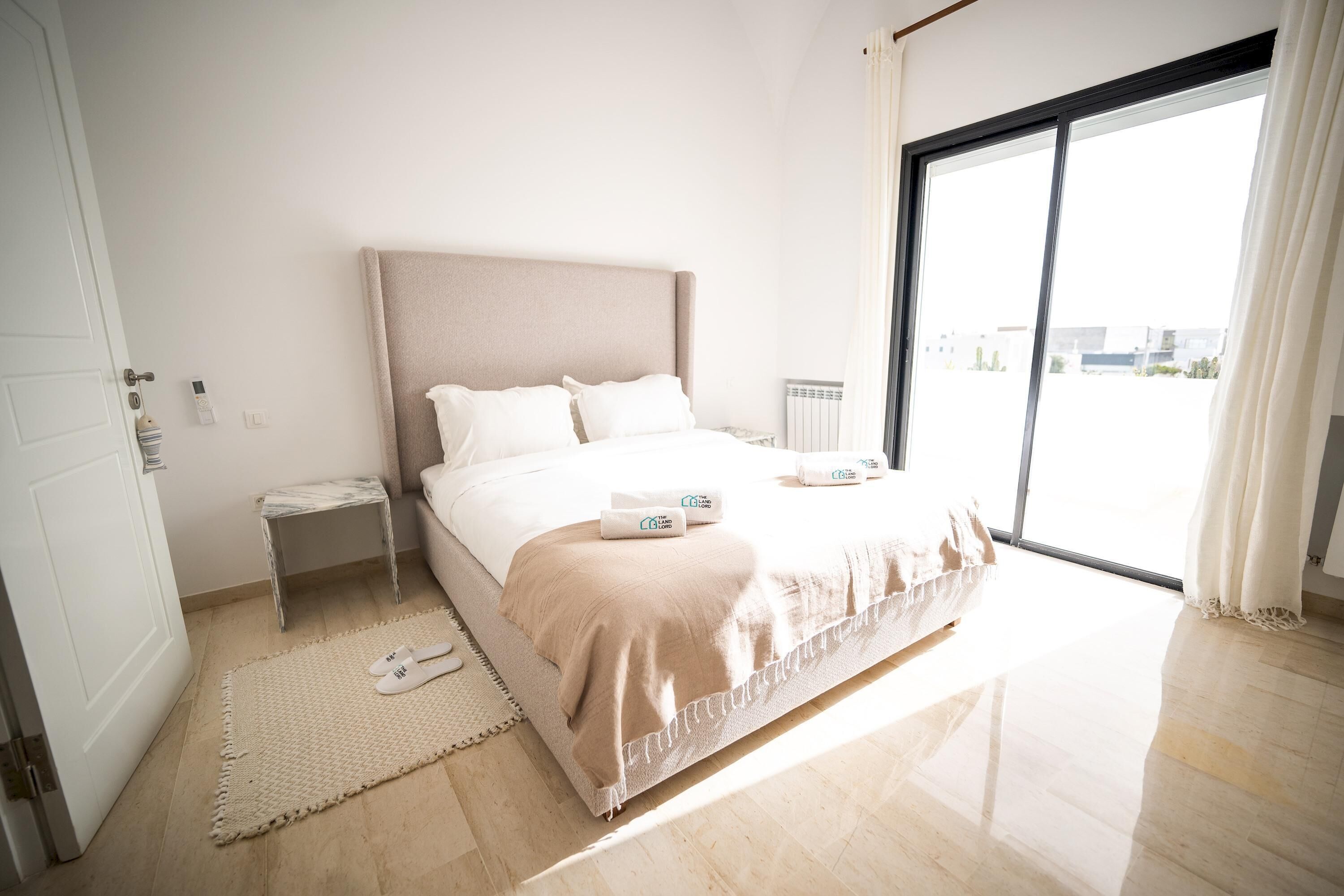 Une chambre d’hôtel moderne avec un grand lit, une petite table de chevet, un radiateur et une vue sur la ville par une grande fenêtre.