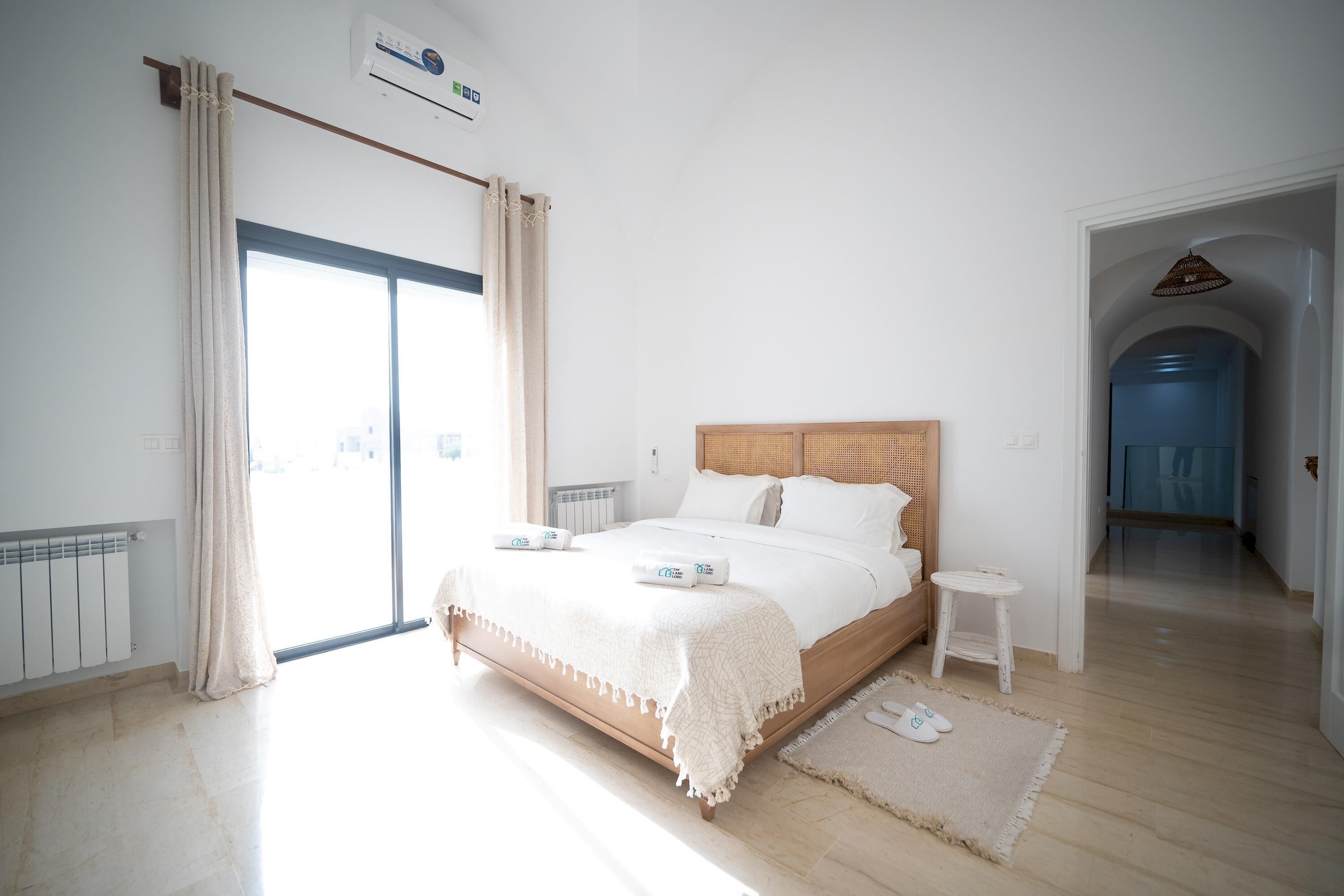 A bedroom with a bed, a small bedside table, a radiator, and a view of the outside.