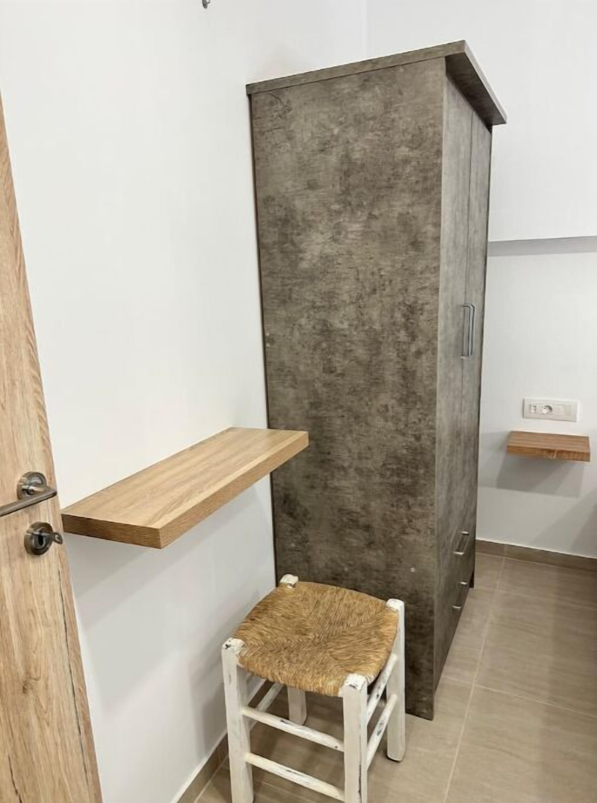 Huoneessa on puinen ovi, korkea kaappi ja pieni jakkara.