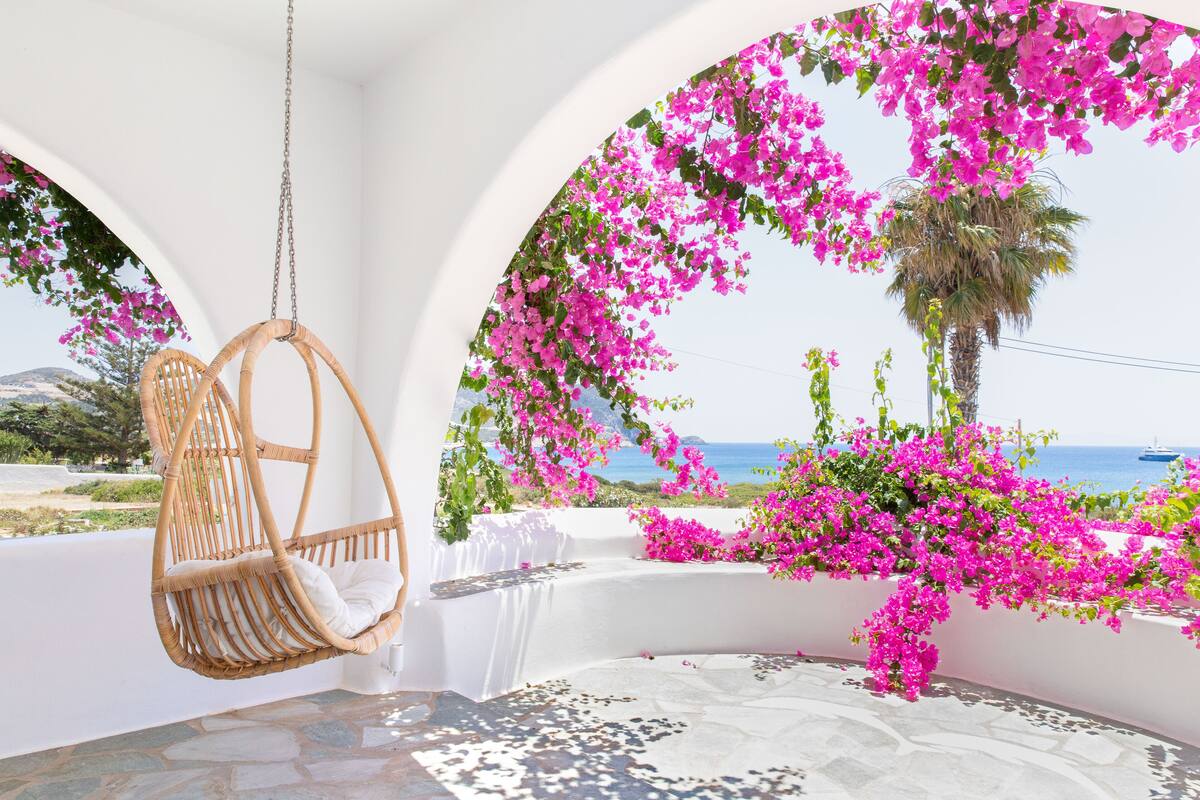 Una silla colgante de mimbre, paredes blancas y flores de buganvilla rosadas.