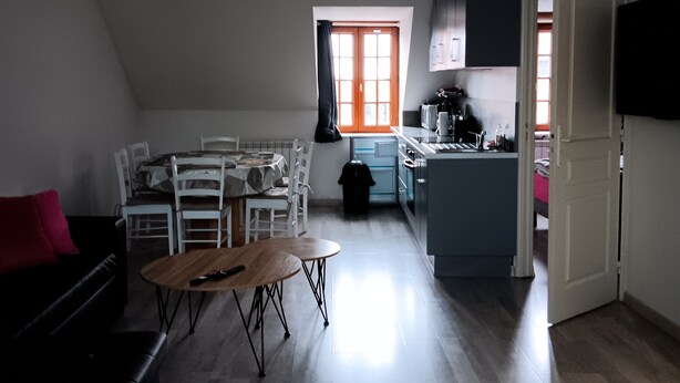 Un'ampia zona giorno con un tavolo da pranzo, un divano nero e una cucina sullo sfondo.