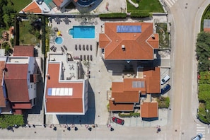 An aerial view of a residential area with a swimming pool, multiple buildings with red-tiled roofs, and a road. - Holiday apartment with air conditioning and outdoor pool (Fažana)