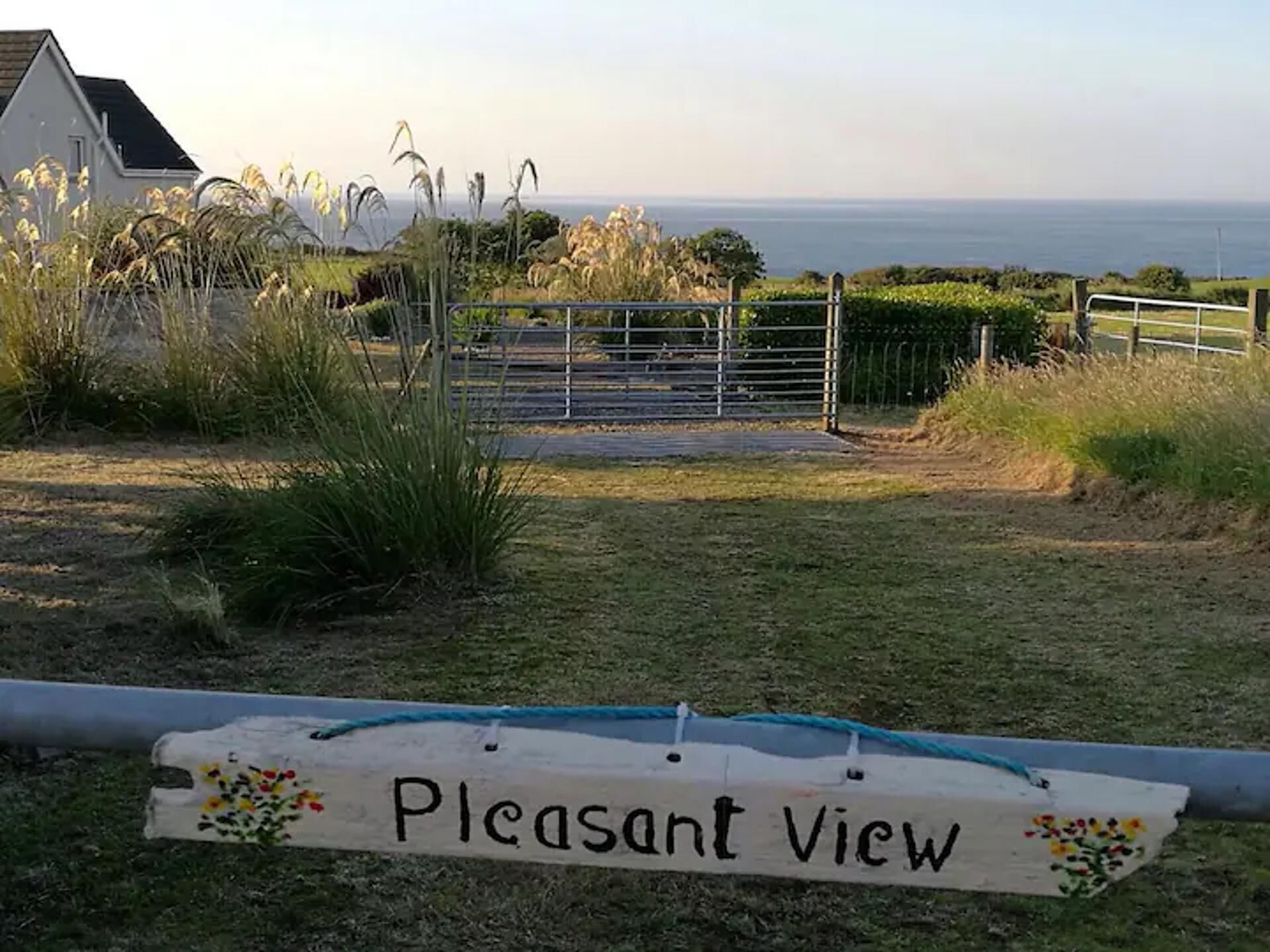 A sign reading "Pleasant View" in front of a gate with a view of the sea.