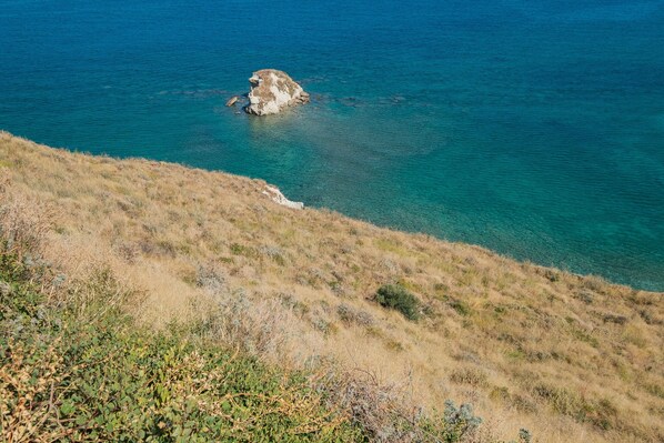 Un paisaje costero con un promontorio rocoso en el mar y una colina cubierta de hierba en primer plano.