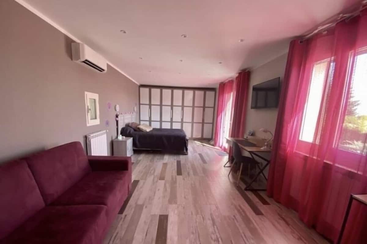 A modern room with a large bed, a red sofa, a desk, and a TV.