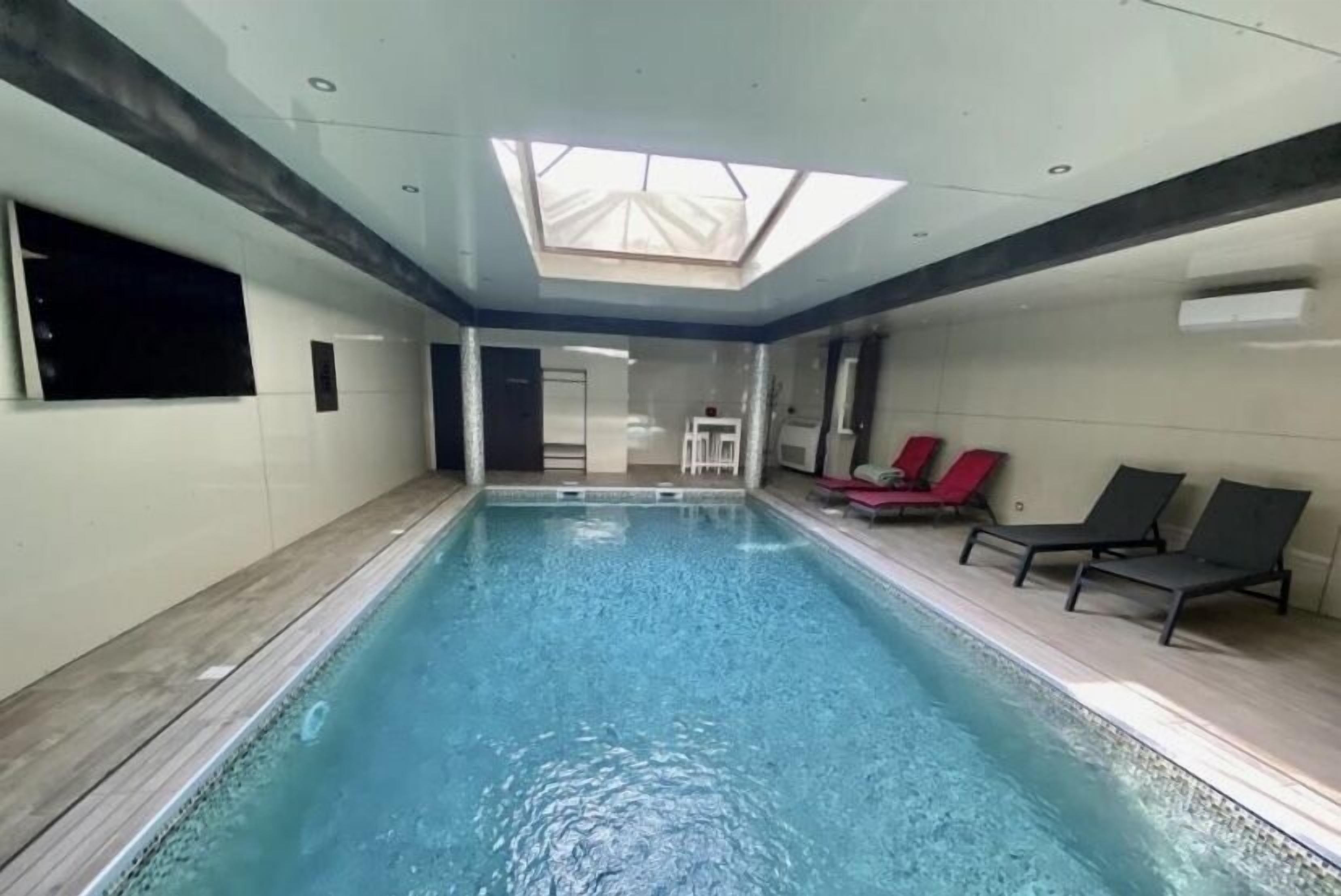 An indoor swimming pool with a skylight, lounge chairs, and a tiled floor.