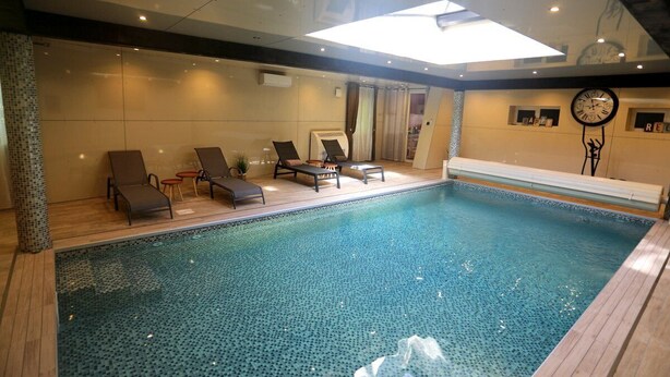 Una piscina interior moderna con sillones de descanso y un techo iluminado por el sol.