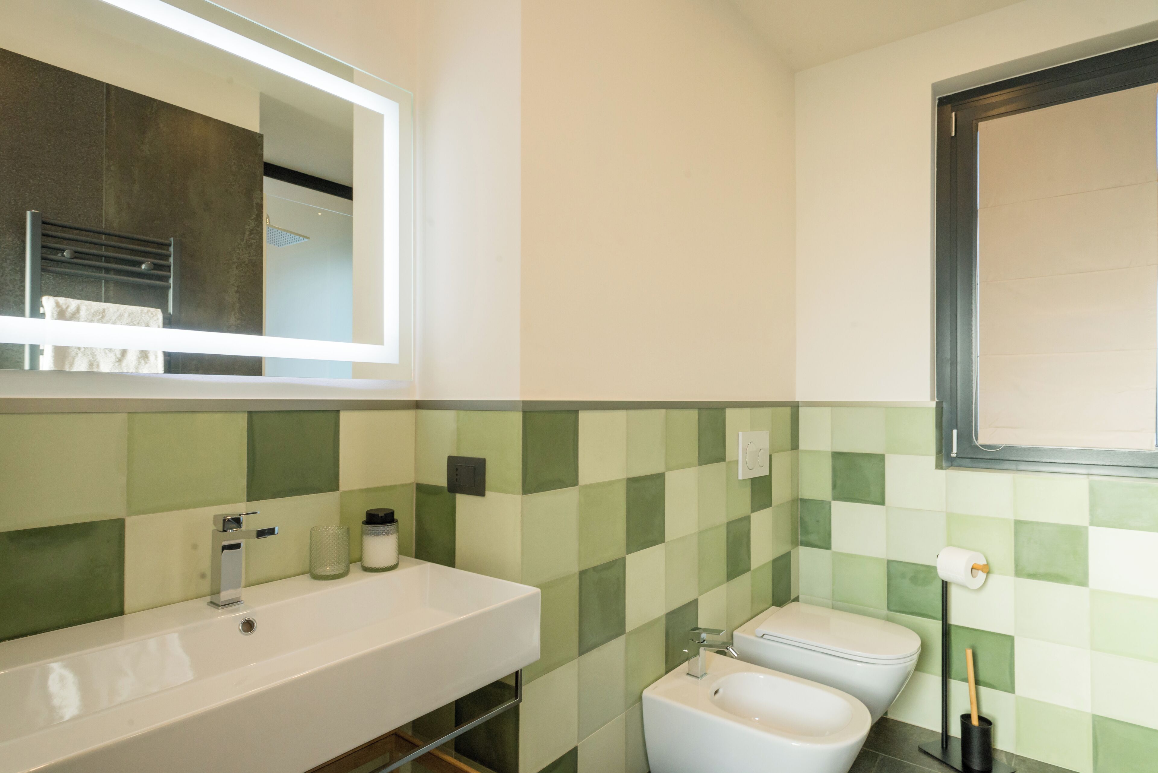 A bathroom with a white sink, a mirror, a toilet, and green checkered tiles.