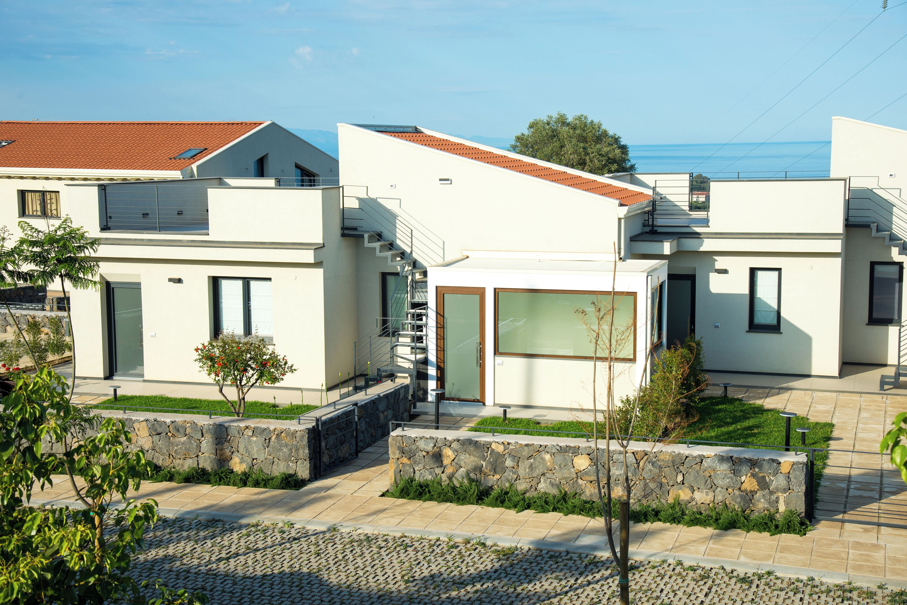 Un edificio residencial moderno con un muro de piedra, un pequeño jardín y una vista despejada al mar.