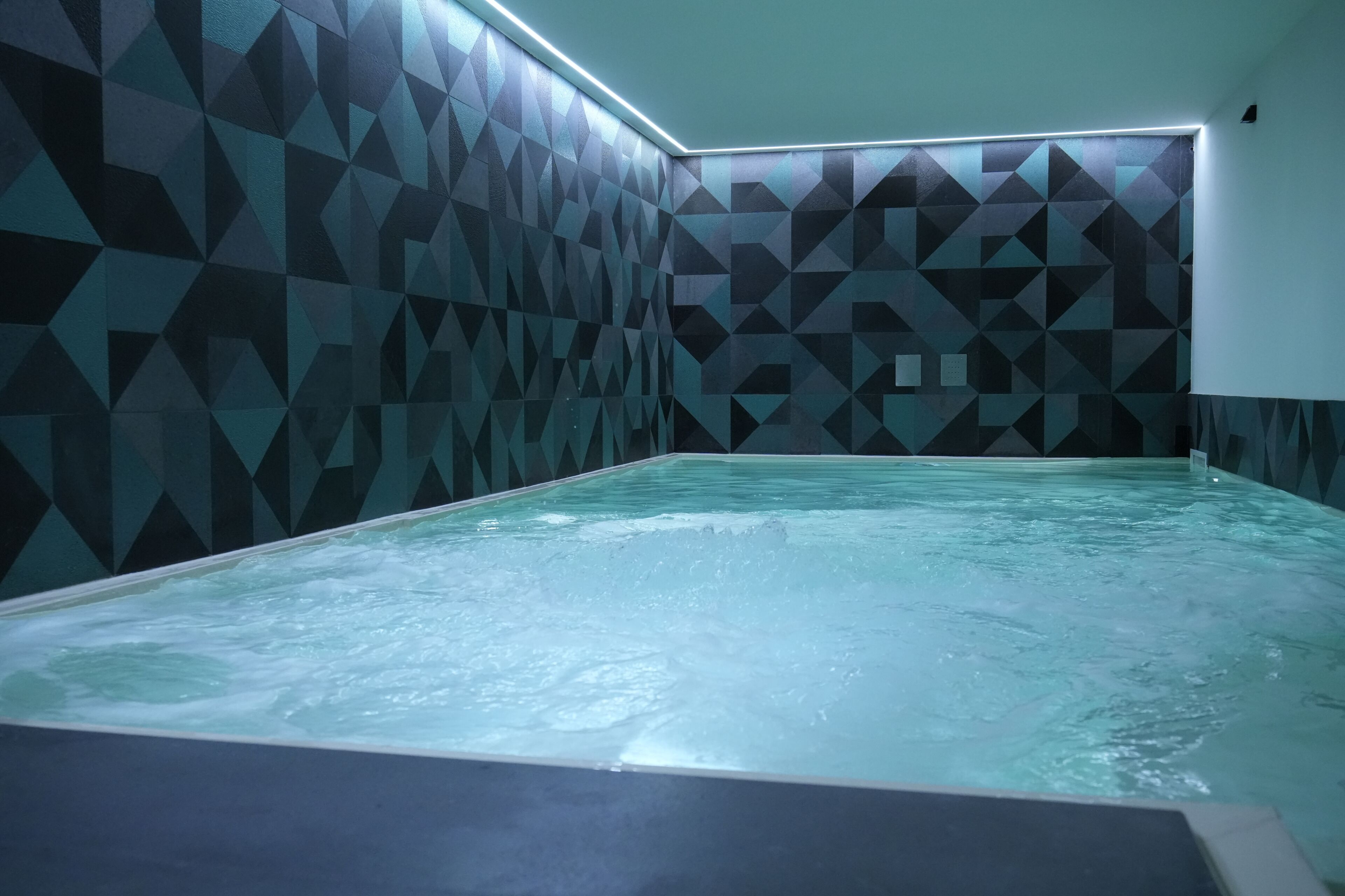 A room with a geometric-patterned wall, a rectangular pool, and a ceiling light.