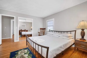 Une chambre à coucher avec un lit, une table de chevet, une lampe et une vue sur une autre pièce.